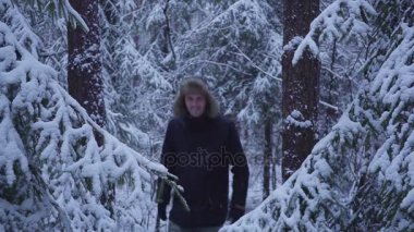 Kar kış orman seyahat sırt çantası ile yürüyen adam. kameraya elini sallayarak