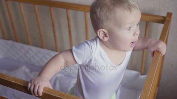 Мальчик в кроватке смотрит вокруг говорит, прыгает и улыбается . — стоковое видео