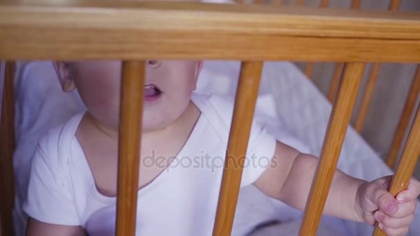 Kid in the crib looks around speaks, jumps and smiles. — Stock Video