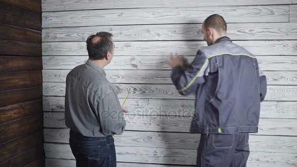 Arbeiter und der anspruchsvolle Kunde, um auf dem Hintergrund einer Holzwand zu diskutieren und zu schwören. Problem im Bauwesen. — Stockvideo