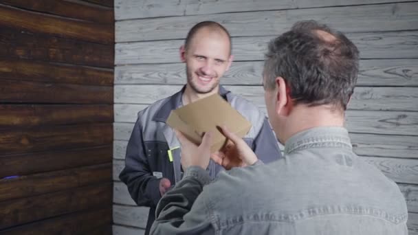 El joven mensajero con uniforme gris trajo un paquete al cliente. . — Vídeos de Stock