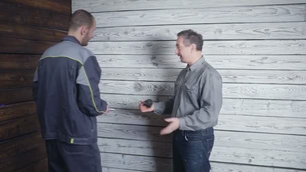 De klant wordt samengevoegd met de bouwer over de herstelling van zijn kamer op de achtergrond van een houten muur. De klant wil hebben een kledingkast — Stockvideo