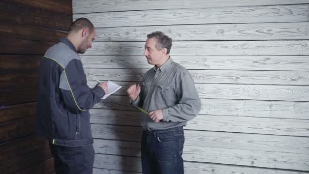 The customer merges with the builder about the repair of his room on the background of a wooden wall. The customer wants to have a wardrobe — Stock Video