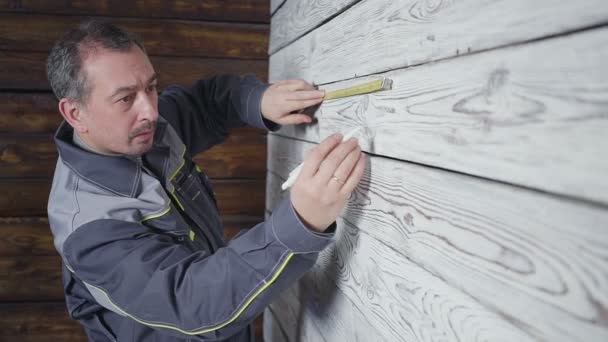 Der Arbeiter misst mit dem Lineal eine Holzwand — Stockvideo