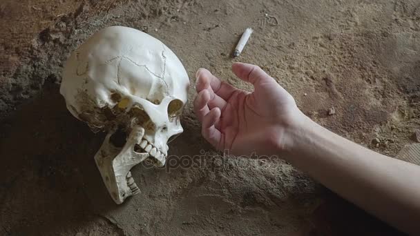 Rauchen tötet Konzept, Hand einer Person, die vor dem Hintergrund des Schädels am Rauchen stirbt — Stockvideo