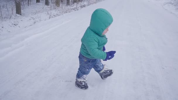 Веселий однорічний хлопчик на зимовій лісовій дорозі. створено з гільзою — стокове відео