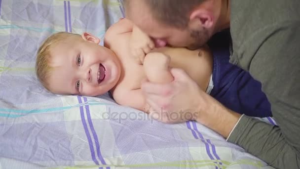 Отец целует, обнимает и щекочет своего маленького сына . — стоковое видео