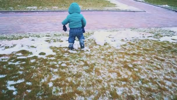 Primavera. Steadicam tiro de niño corriendo por la acera, hierba y nieve derretida. cámara lenta — Vídeos de Stock
