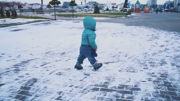 Primavera. Steadicam tiro de niño corriendo por la acera, hierba y nieve derretida. cámara lenta — Vídeo de stock