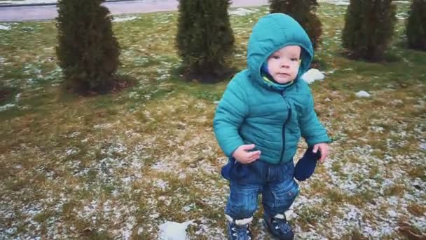 Lente. Kid draait de stoep, gras en smeltende sneeuw. — Stockvideo