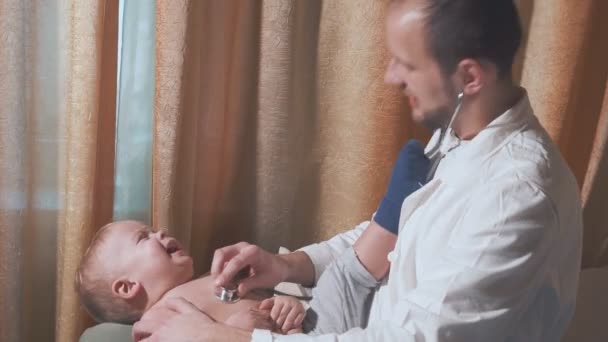 Врач навещает малыша дома. Ребенок плачет и доктор со стетоскопом — стоковое видео