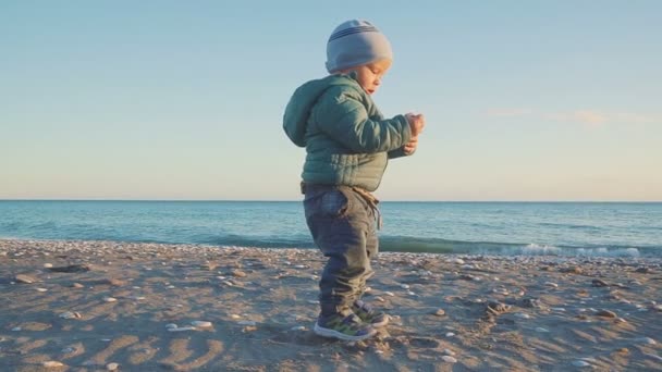 Estilo de vida do bebé. Um menino é jogado com areia e pedras em uma praia natural — Vídeo de Stock