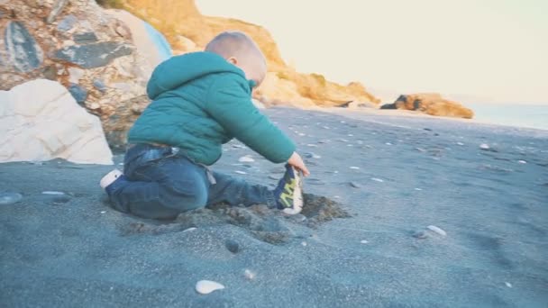 Stile di vita del bambino. Un ragazzo è giocato con sabbia e pietre su una spiaggia naturale — Video Stock