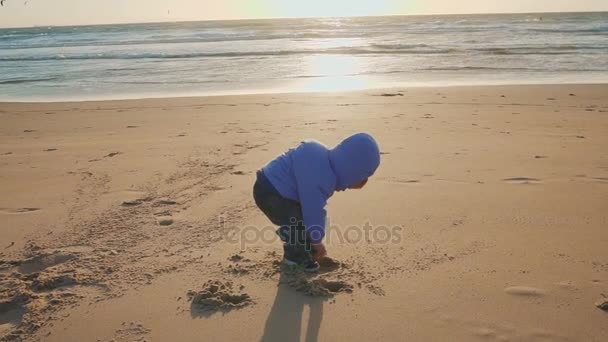 De levensstijl van de baby. Een jongen wordt gespeeld met zand en stenen op een natuurlijke strand — Stockvideo