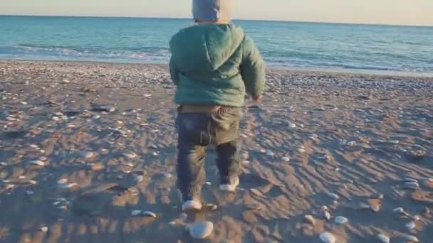 De levensstijl van de baby. De jongen loopt naar de zee bij zonsondergang. concept vakantie. — Stockvideo