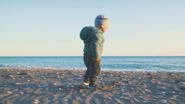 Een één jaar oude jongen loopt en is gespeeld op het strand in de buurt van de zee — Stockvideo