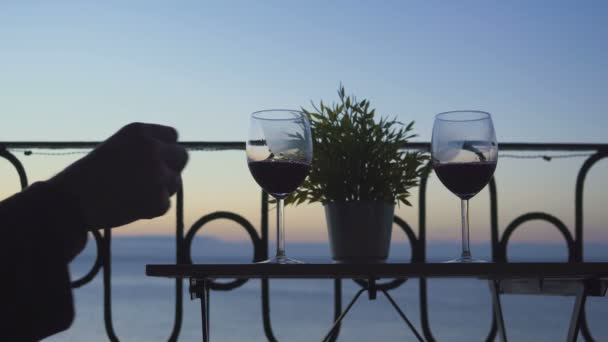 Un uomo e una donna sono seduti sul balcone e bevono vino rosso sullo sfondo del mare. Primo piano . — Video Stock