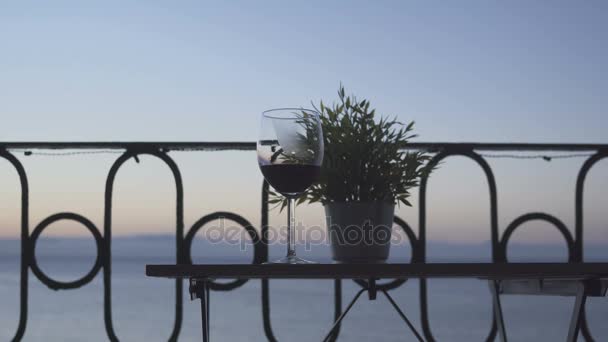 Ein Mann sitzt auf dem Balkon und trinkt Rotwein vor dem Hintergrund des Meeres. Nahaufnahme. — Stockvideo
