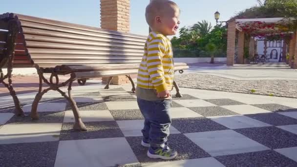 Sunny summer. Steadicam shot of baby boy running down the sidewalk, slow motion — Stock Video