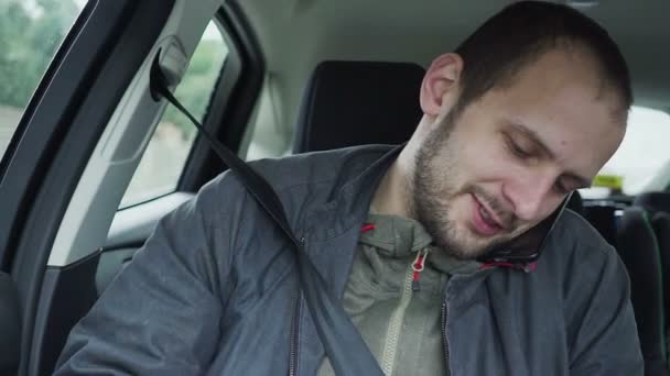 Крупный план молодой человек разговаривает по мобильному телефону во время езды на заднем сиденье автомобиля — стоковое видео