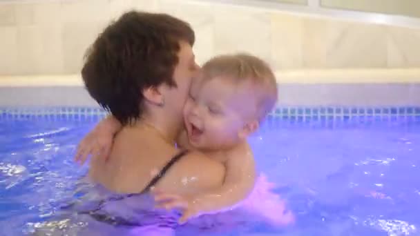 Uma jovem mãe com um menino nada e se diverte na piscina. Menino feliz está nadando na piscina junto com sua mãe — Vídeo de Stock