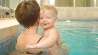 Erkek bir bebek ile genç bir anne yüzüyor ve havuzda eğlenceli. Mutlu küçük çocuk annesi ile birlikte havuzda yüzüyor
