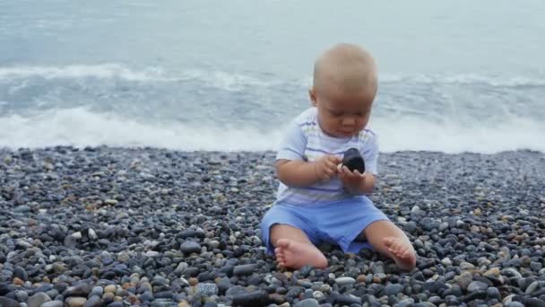 Новонароджений хлопчик грає на вітряному узбережжі з камінням — стокове відео