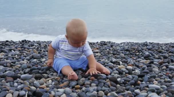 Neugeborener Junge spielt am windigen Meer mit Steinen — Stockvideo