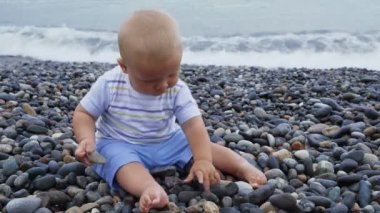 Yeni doğan bebek çocuk taşlarla rüzgarlı deniz kenarında oynuyor