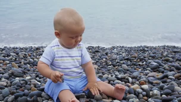 Новонароджений хлопчик грає на вітряному узбережжі з камінням — стокове відео