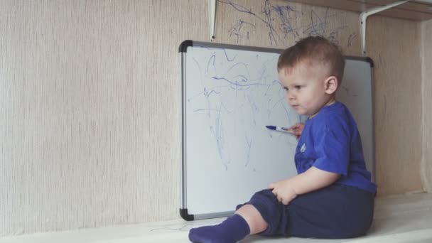 Baby vergadering op de vensterbank en trekt op Markeringsbord. — Stockvideo