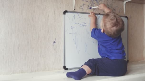 Bebê sentado no peitoril e desenha no quadro marcador . — Vídeo de Stock