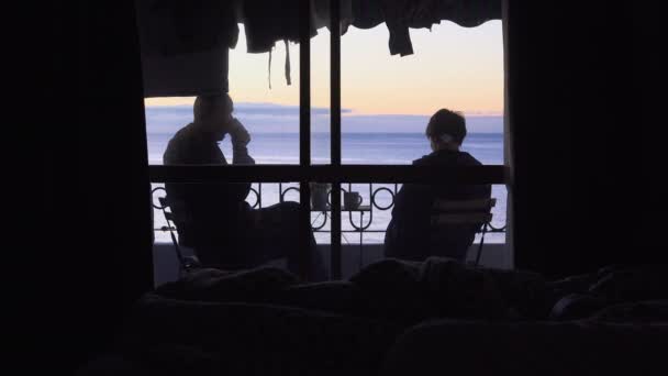 Μια νεαρή γυναίκα και άντρας κοιτάζει την Ανατολή του ηλίου στη θάλασσα από το ξενοδοχείο μπαλκόνι και να πιείτε καφέ — Αρχείο Βίντεο