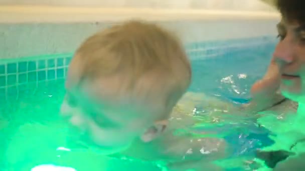 Молодая мать с маленьким мальчиком плавает и веселится в бассейне. Счастливый маленький мальчик плавает в бассейне вместе со своей матерью — стоковое видео