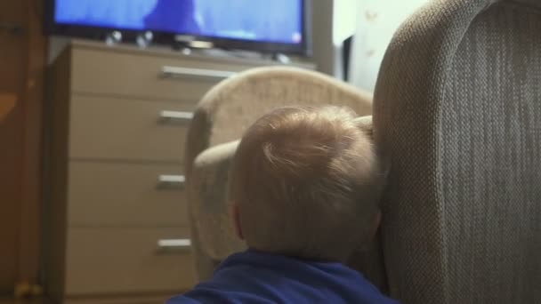 One year old child watching TV - dolly shot. Little boy watching cartoon on tv in the room. — Stock Video