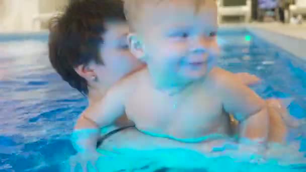 Uma jovem mãe com um menino nada e se diverte na piscina. Menino feliz está nadando na piscina junto com sua mãe — Vídeo de Stock