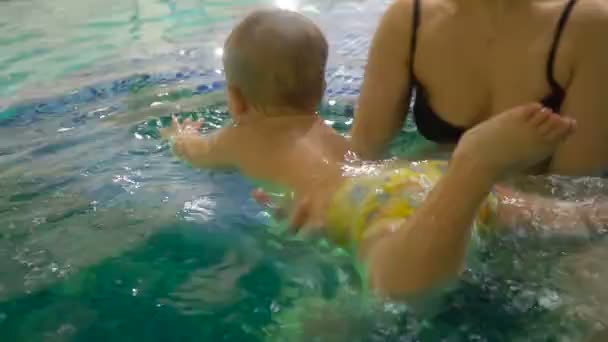 Uma jovem mãe com um menino nada e se diverte na piscina. Menino feliz está nadando na piscina junto com sua mãe — Vídeo de Stock