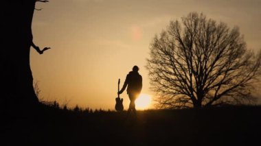 Gitarist günbatımı yavaş hareket, silüeti. Onun elinde gitar gitarist yürür