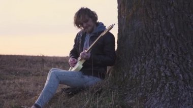 adam elektro gitar tree yakınındaki bir alanda gün batımında çalış.