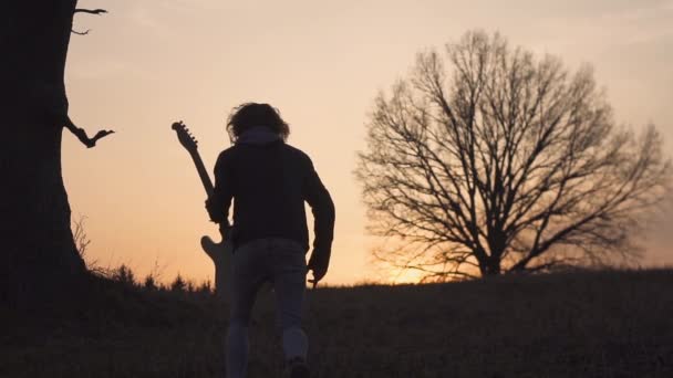 Silueta del guitarrista al atardecer en cámara lenta. corre con una guitarra en sus manos — Vídeos de Stock