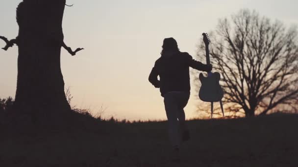 Silhouette des Gitarristen bei Sonnenuntergang in Zeitlupe. läuft mit einer Gitarre in der Hand — Stockvideo