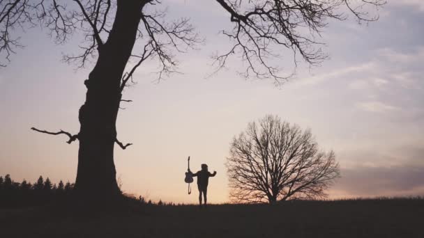 Σιλουέτα του κιθαρίστα στο ηλιοβασίλεμα αργή κίνηση. τρέχει με μια κιθάρα στα χέρια του — Αρχείο Βίντεο