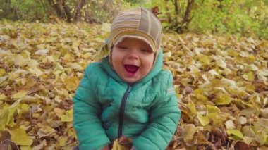 Park düşen yaprakları ile oynarken mutlu bebek boy gülümseyerek. ağır çekim
