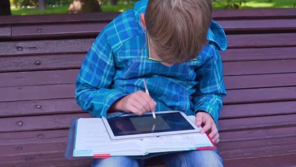 A hallgató, aki csinál házi feladatot a tankönyv és a tabletta, a szabadban portréja — Stock videók