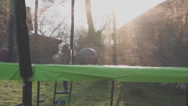 Brother and sister playing on the field at the evening time. People having fun outdoors. They jumping on trampoline on the lawn. Concept of friendly family. Slow motion — Stock Video