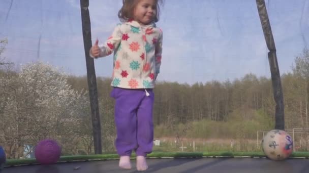 Gelukkig drie jaar oud meisje en springen op een trampoline. Emotionele vrolijke portret. Slow motion — Stockvideo