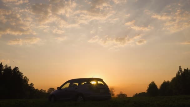 Silhuetten av en bil i ett fält vid solnedgången. Vägen och fältet. Bilen på fältet. — Stockvideo