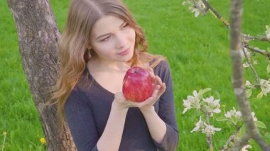 güzel kız bir elma bir elma bahçesi zemin karşı onun elinde. Bir kadın bir elma yemek istiyor. Bahçe çiçek açan bir bahçeye sahip. Meyve ağaçları çiçekleri.