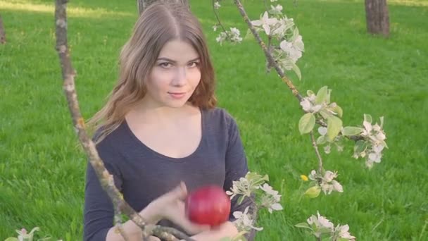 Портрет обличчя молодої красивої жінки, що тримає яблуко на весняному квітучому яблуні на фоні літньої природи. весняний сезон — стокове відео