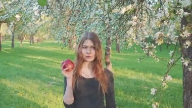 güzel kız bir elma bir elma bahçesi zemin karşı onun elinde. Bir kadın bir elma yemek istiyor. Bahçe çiçek açan bir bahçeye sahip. Meyve ağaçları çiçekleri.